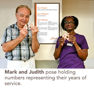 Mark and Judith pose holding numbers representing their years of service