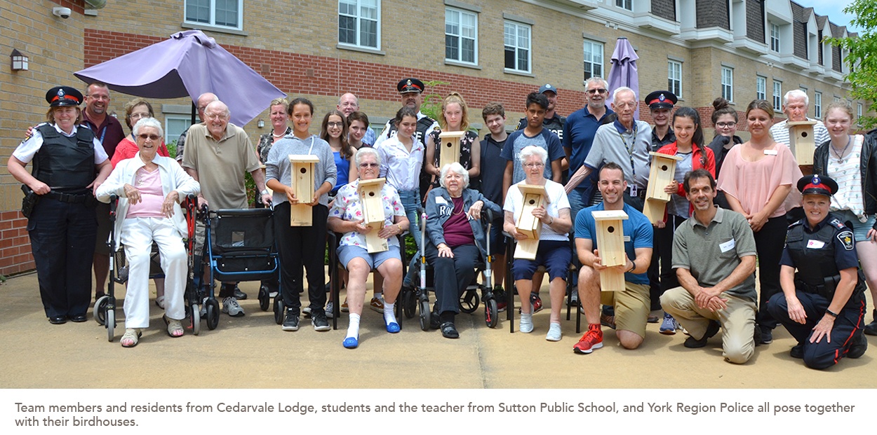 Team members and residents from Cedarvale Lodge, students and the teacher from Sutton Public School, and York Region Police all pose together with their birdhouses.