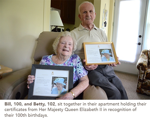 Bill, 100, and Betty, 102, sit together in their apartment holding their certificates from Her Majesty Queen Elizabeth II in recognition of their 100th birthdays.
