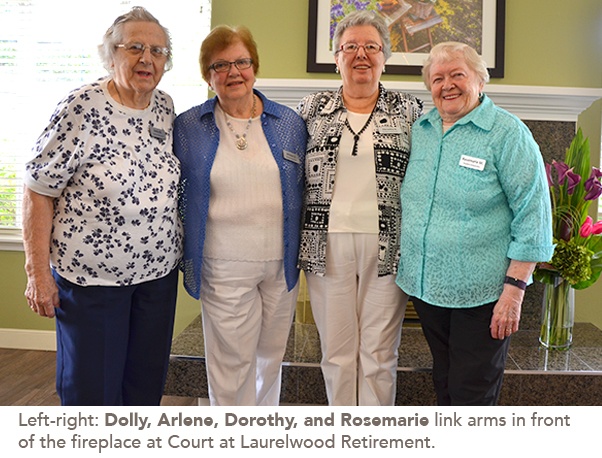 Photo of Dolly, Arlene, Dorothy, and Rosemarie link arms in front of the fireplace at Court at Laurelwood Retirement.