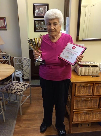 A female senior is holding a trophy and an award certificate